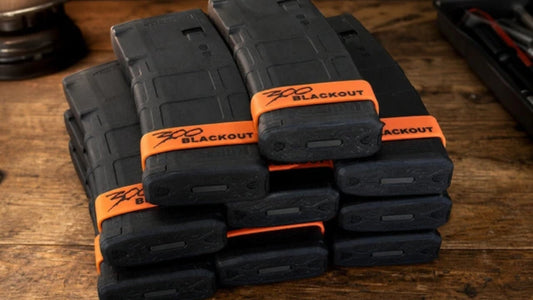 Black AR magazines banded with orange SPARTA 300 Blackout bands, stacked on a wood bench