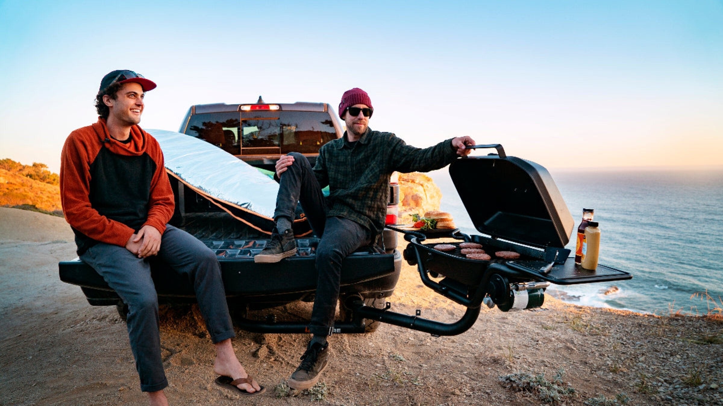 A HitchFire grill swung out off the back of a pickup, burgers on the grate.